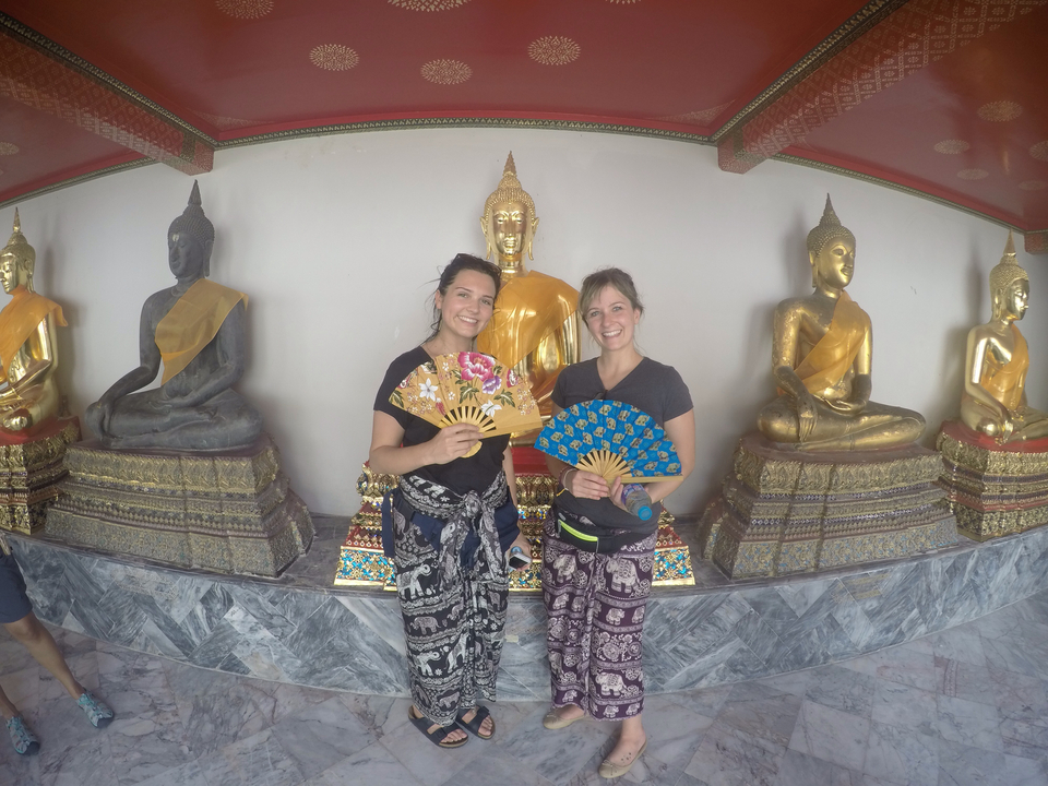 Two women standing in front of golden Buddha statues.