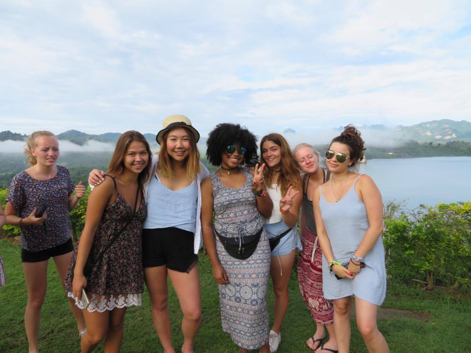 Group of young women posing with a scenic hill and lake view.