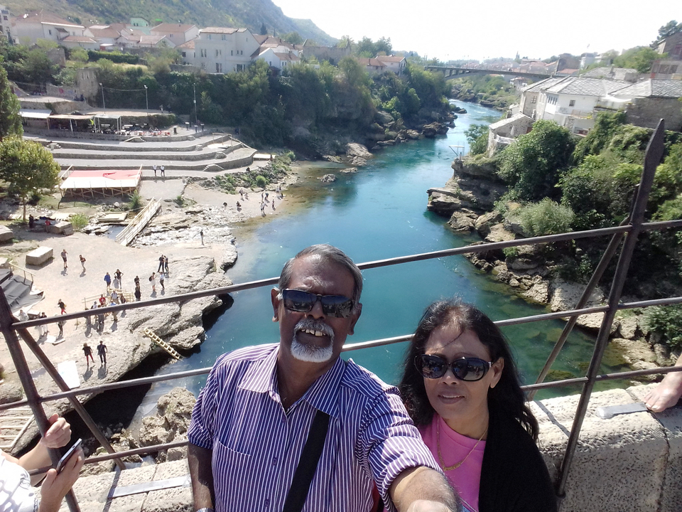 Couple prenant un selfie au bord d'une rivière avec une ville pittoresque en arrière-plan.