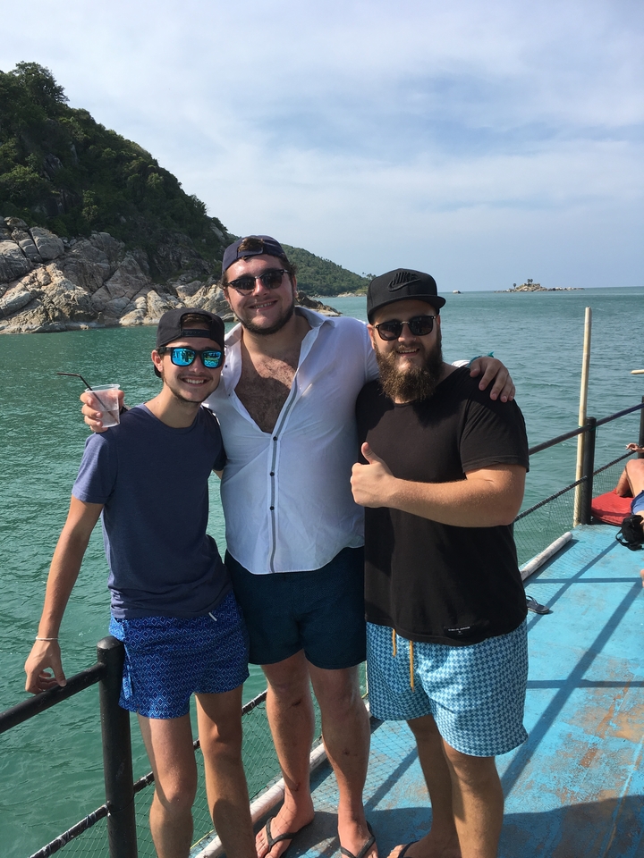 Three friends posing on a boat with water and cliffs in the background.