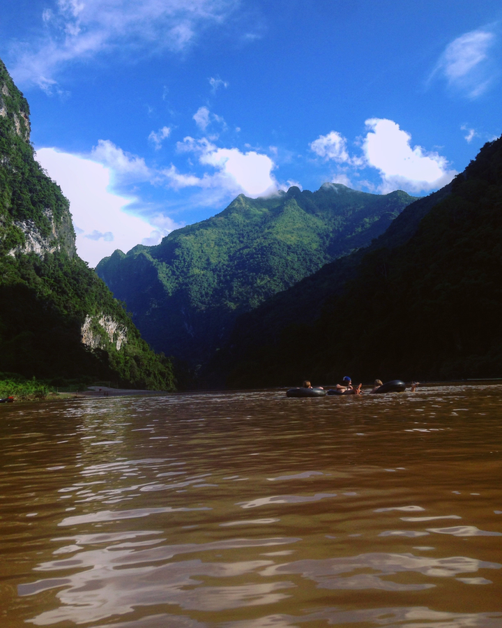 People floating in a river with green mountains.