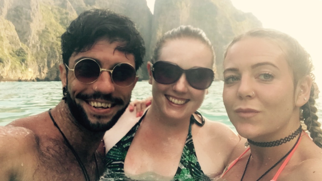 Three people in swimming attire with cliffs in the background.