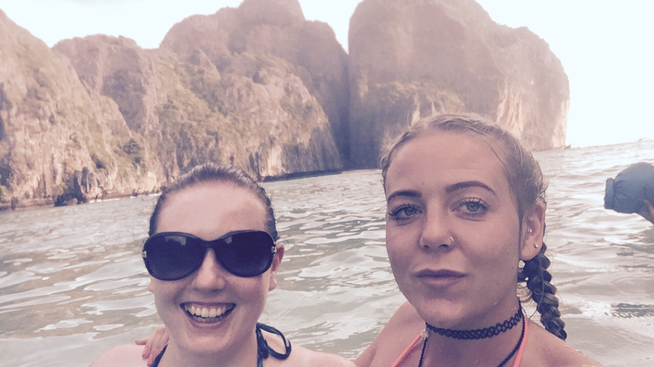 Two people in swimming attire in the sea with cliffs.