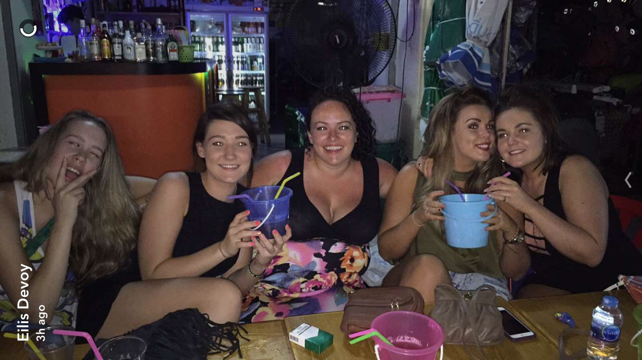 Group of women having drinks in a bar with vibrant lighting and a watermark.