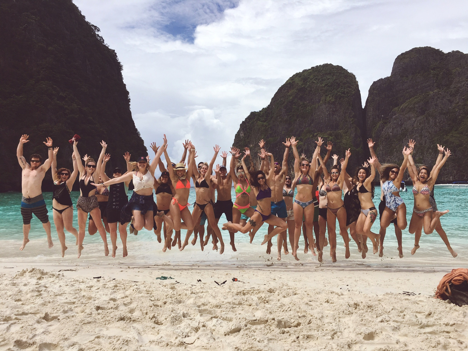 Group of friends jumping on the beach with scenic cliffs.