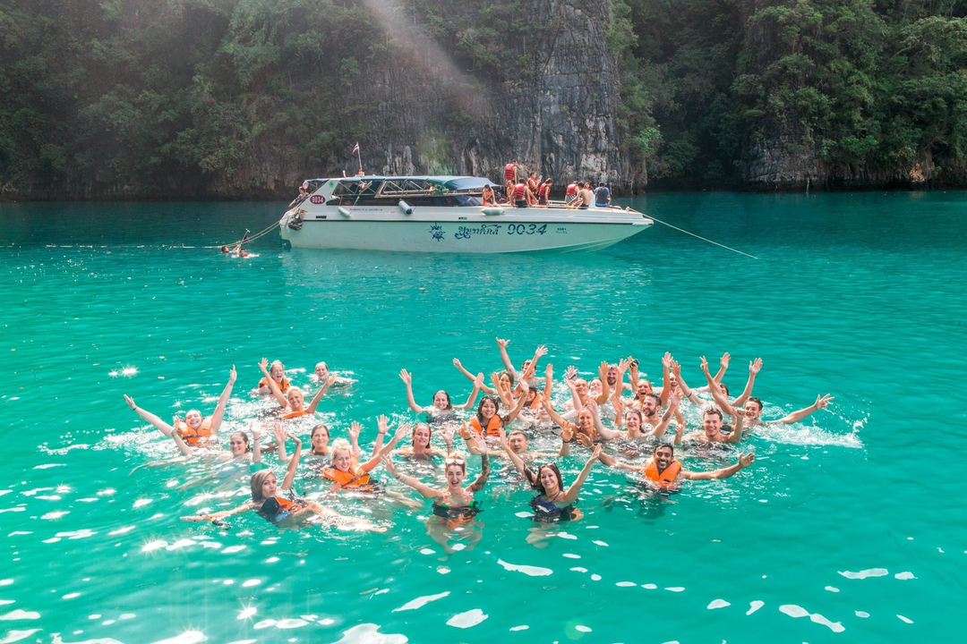 Group of people in the sea making a circle, with a boat in the background.
