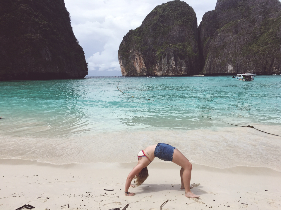 Person doing a backbend on the beach with clear water.