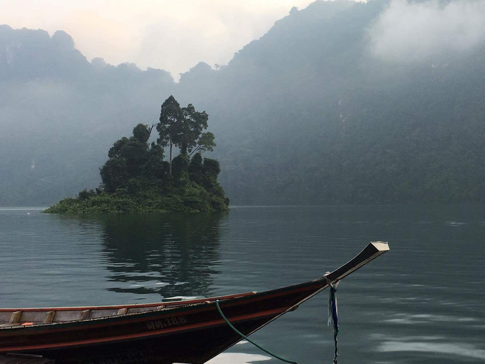 Boat on a calm lake with a misty island in the backdrop.