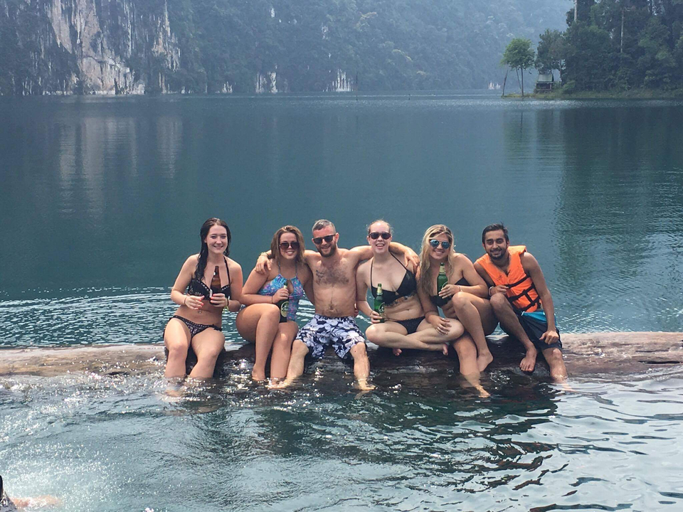 Group of friends sitting by water, enjoying drinks.
