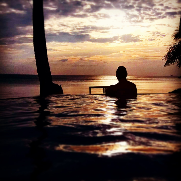 Silhouette of a person relaxing in an infinity pool at sunset.