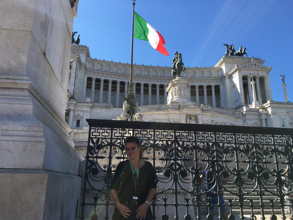 Person posing in front of the Altare della Patria with an Italian flag.
