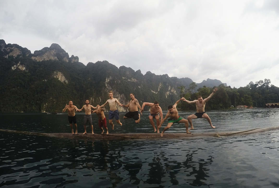 Group of people jumping into a lake surrounded by mountains.