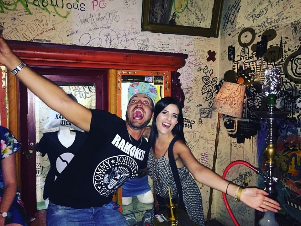 Two people inside a graffiti-covered room posing with smiles.