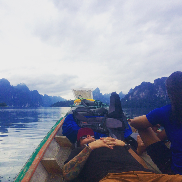 Two people relaxing at the front of a boat in a scenic lake with limestone hills.