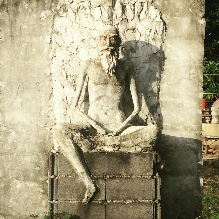 Stone sculpture of a seated figure against a wall.