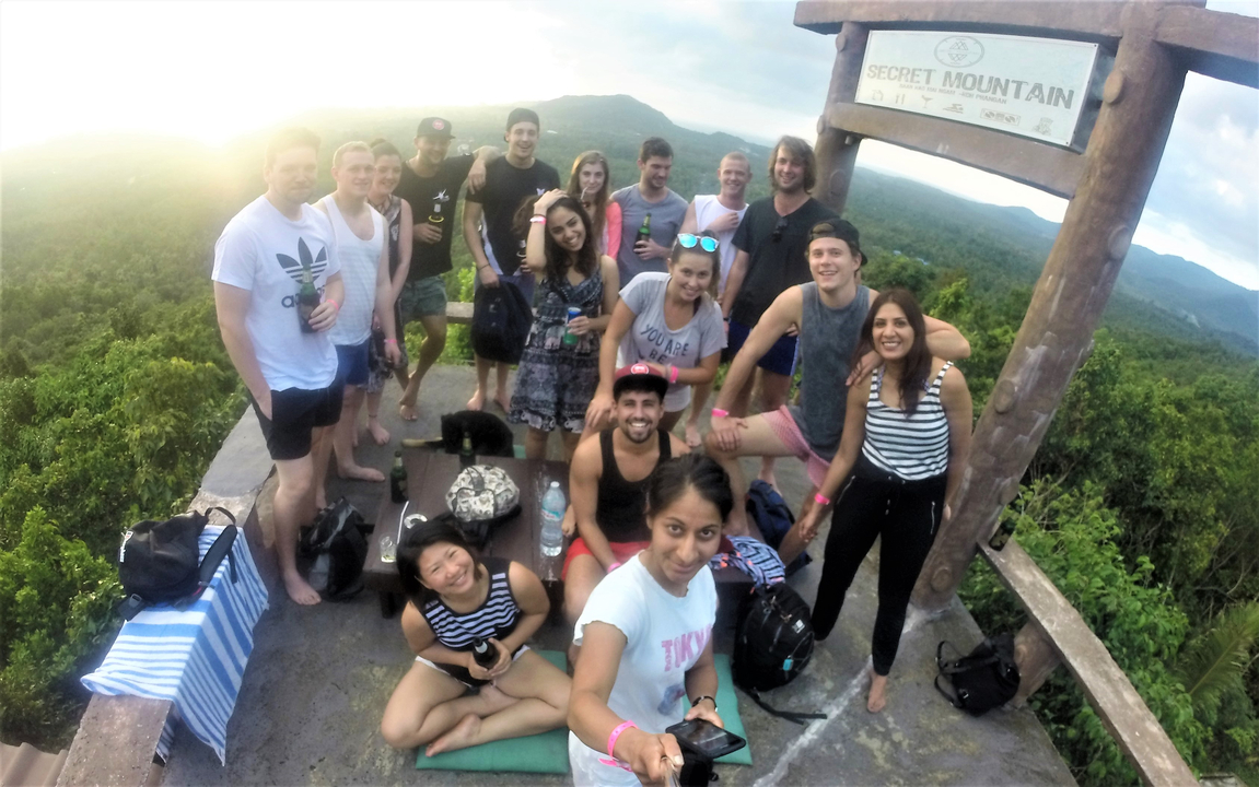 A large group posing on a mountain summit with a sign.