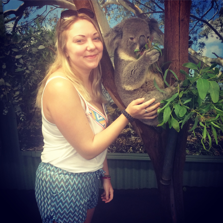A person posing with a koala bear in a tree.