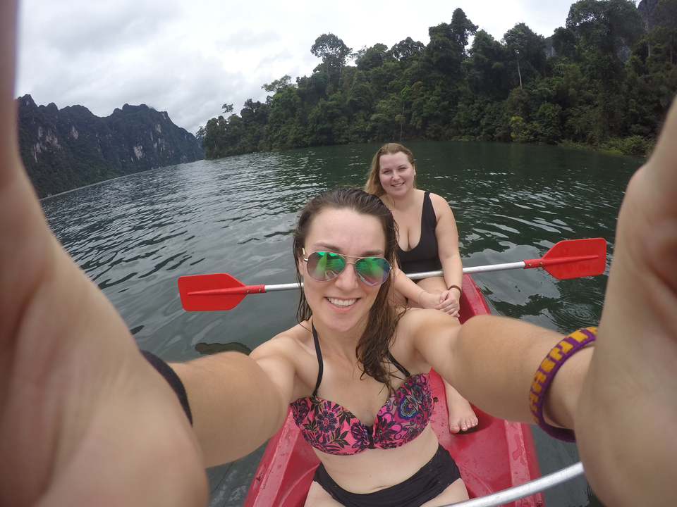 Two women posing on a kayak in a lake with mountains.