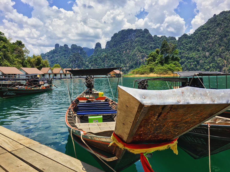 Long-tail boats docked on a tropical lake with limestone cliffs.