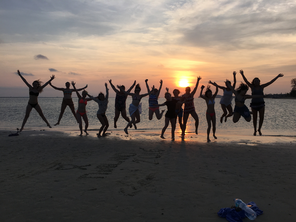 A group of people jumping on a beach during sunset.