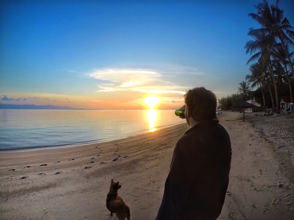 Person on a beach with a drink, watching a sunset.