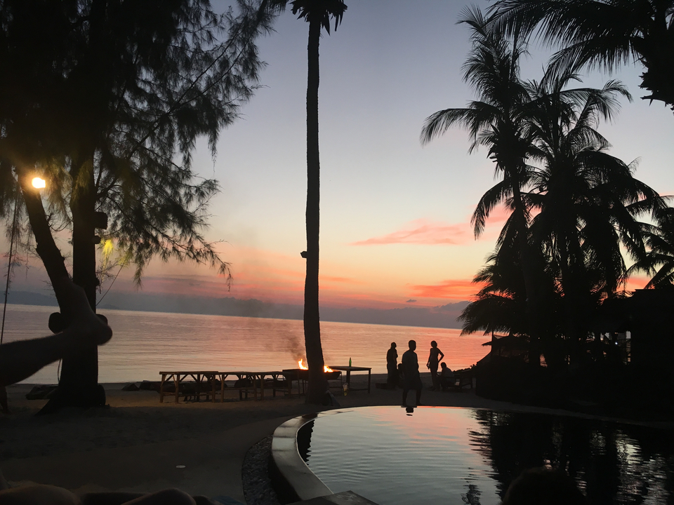 Silhouettes of people on a beach with a bonfire at sunset.