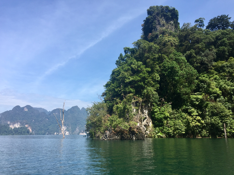Lush green island on a calm lake with a mountainous backdrop.