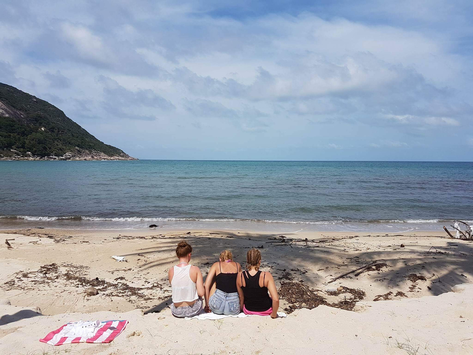 Three people sitting on a beach facing the sea.