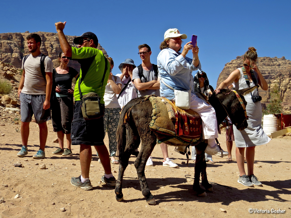 Group of tourists, one riding a donkey near a rocky terrain.