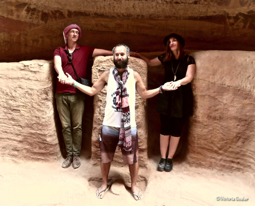 Three people posing in a rock-cut structure, holding hands.