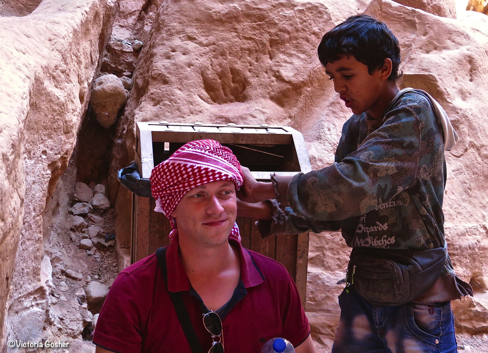 Person having a traditional headscarf adjusted by another.