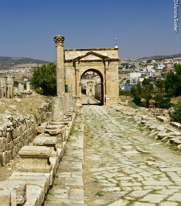 Ancient archway leading to ruins with a city in the distance.