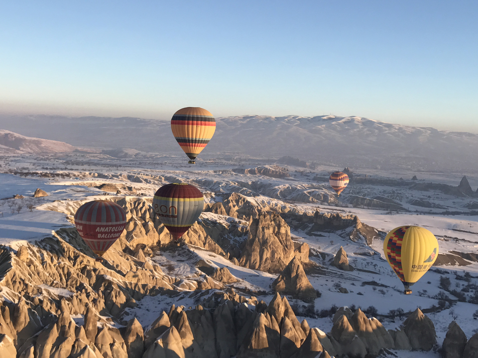 Hot air balloons flying over snowy Cappadocia landscape.