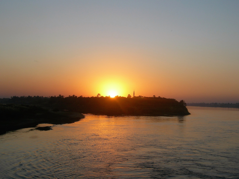Scenic sunset over a calm river and distant trees.