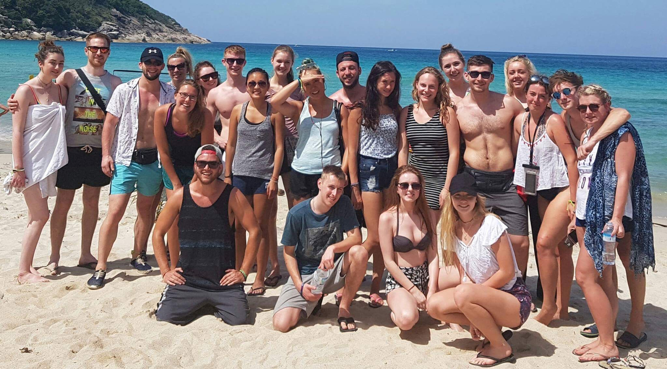 Group of people posing on a beach with mountains in the background.