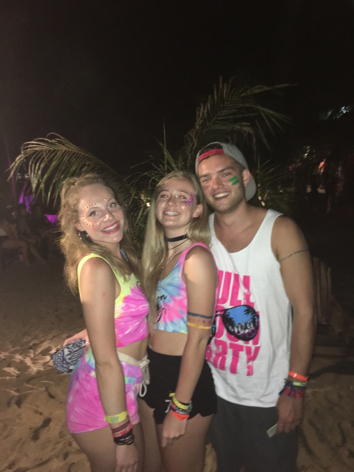 Three people with neon face paint at a night event.