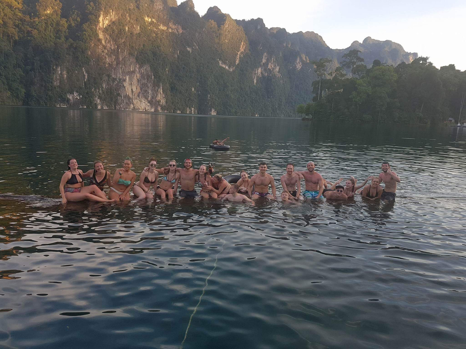 Group of people sitting in the water with a cliff background.