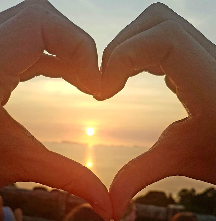Hands forming a heart shape with a sunset in the background.