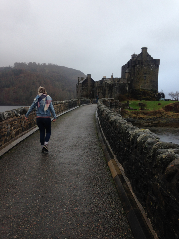 Person walking on a stone bridge towards a historic castle.