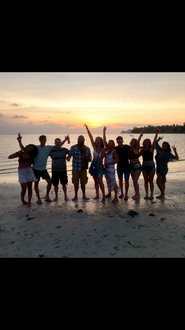 Silhouettes of people on a beach at sunset holding drinks.