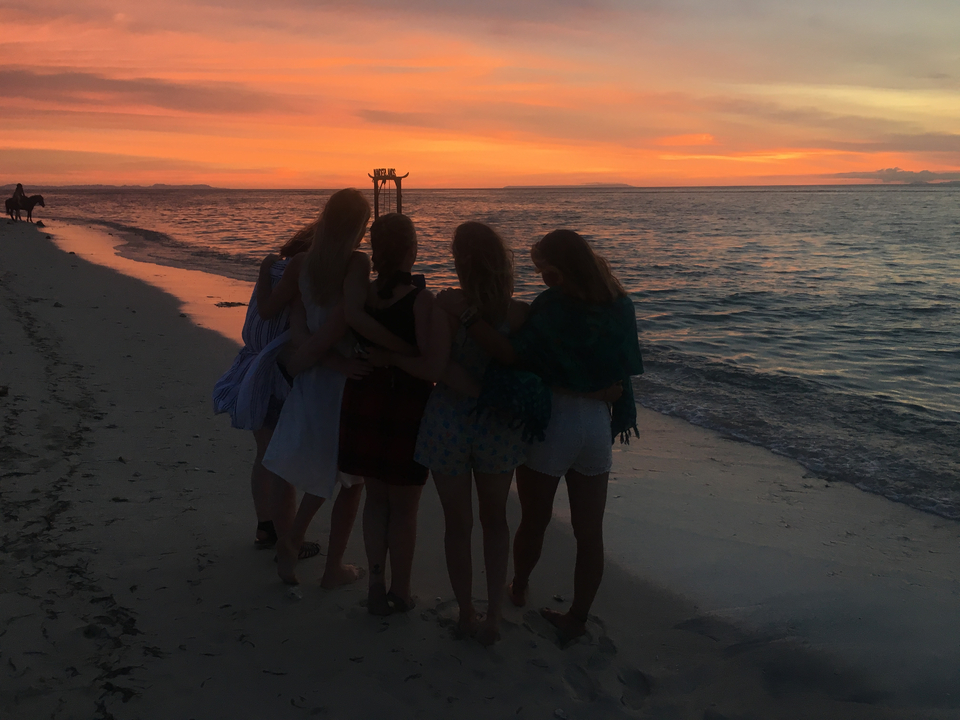Five people huddled together watching a sunset on a beach