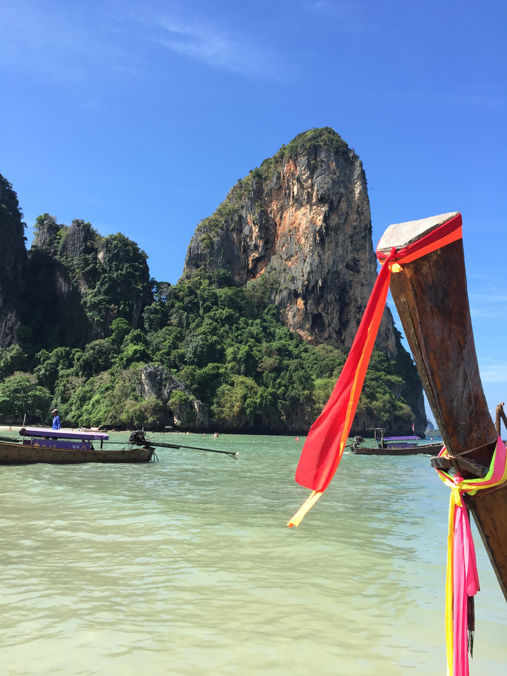 Longtail boats on turquoise water with a towering cliff.