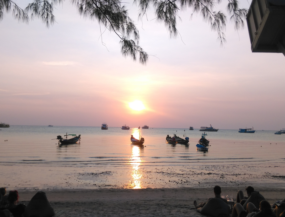 Serene sunset over a beach with small boats on the water.
