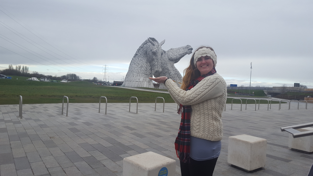 Woman posing with The Kelpies horse sculpture.