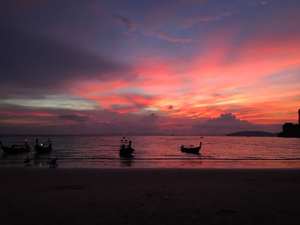 Sunset over the ocean with longtail boats in silhouette.