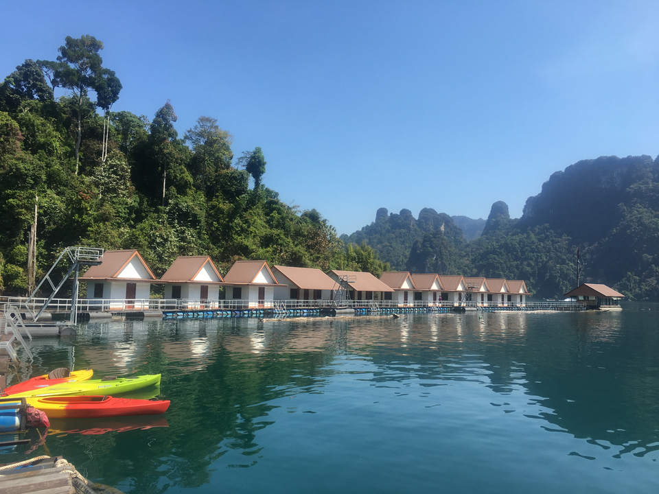 Row of floating bungalows on a lake with limestone cliffs.