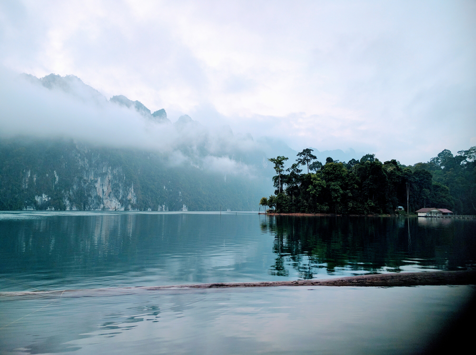 Serene lake reflecting misty mountains in the distance.