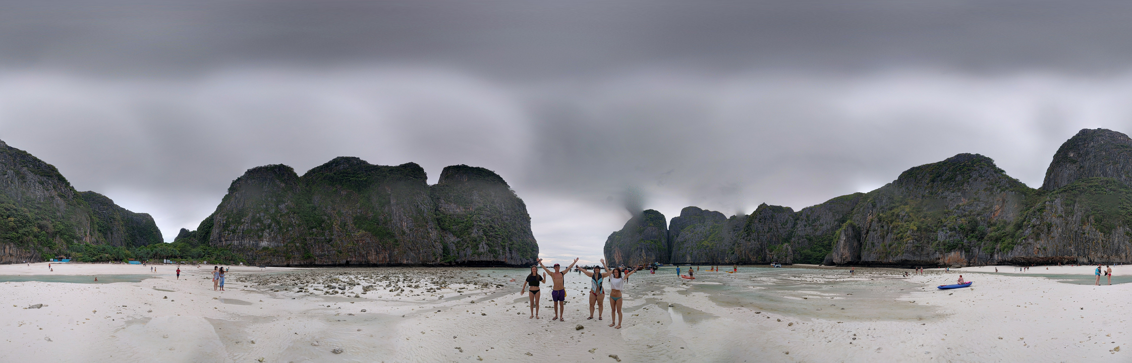 People posing and enjoying a beach with cloudy skies.