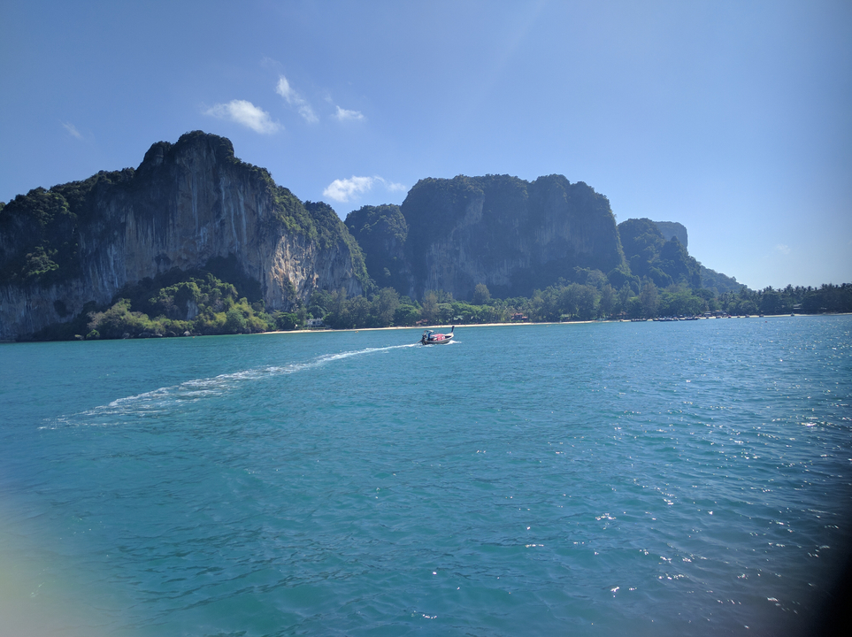 Speedboat on clear waters with towering cliffs in the background.