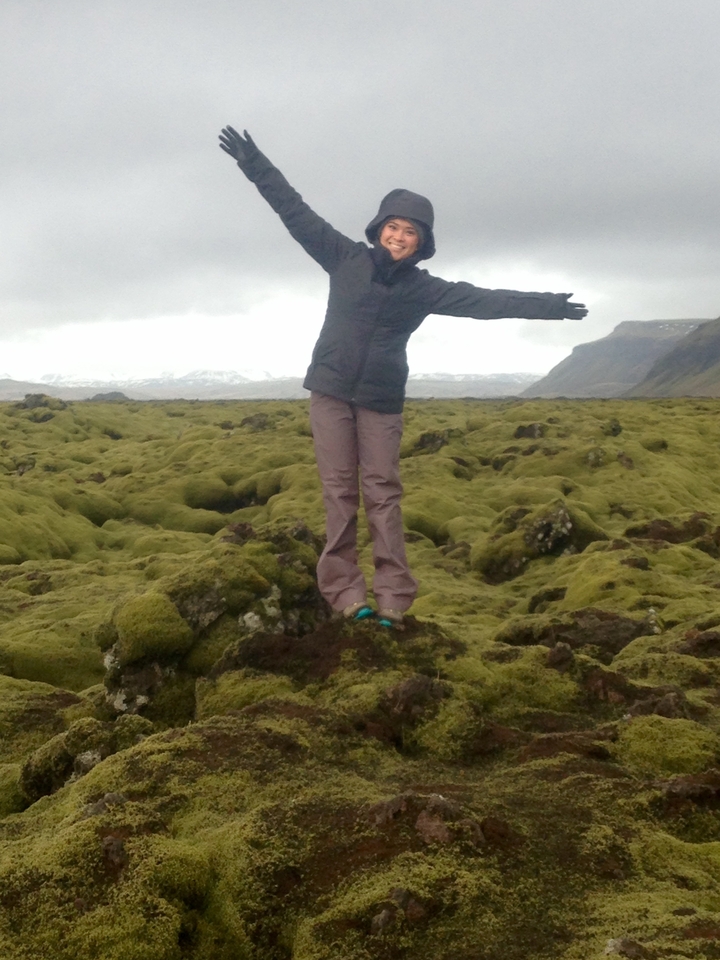 Person with outstretched arms on a moss-covered landscape.